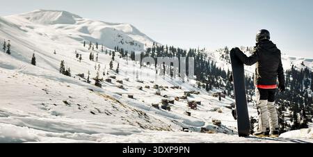 Männlicher Snowboarder in dunkelschwarzem Sportswear Stand gekleidet Genießen Sie das Panorama der Skigebietslandschaft auf Berghang in Georgien Skiurlaubsziel - Stockfoto