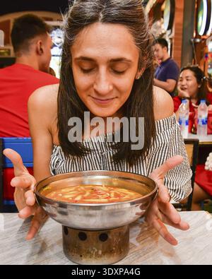 Bangkok, Thailand - 11. februar 2024: kaukasische Frau, Touristen riecht probieren Sie das beliebte thailändische Gericht Tom Yum, heiße Suppe mit Garnelen unter Einheimischen in berühmten ri Stockfoto
