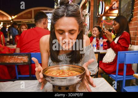 Bangkok, Thailand - 11. februar 2024: kaukasische Frau, Touristen riecht probieren Sie das beliebte thailändische Gericht Tom Yum, heiße Suppe mit Garnelen unter Einheimischen in berühmten ri Stockfoto