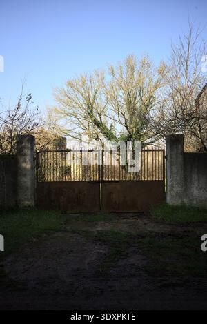 Geschlossenes rostiges Tor in einer Betonmauer, die zu einem Garten führt, auf dem italienischen Land Stockfoto