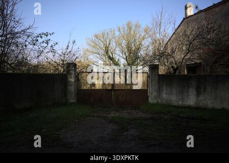 Geschlossenes rostiges Tor in einer Betonmauer, die zu einem Garten führt, auf dem italienischen Land Stockfoto