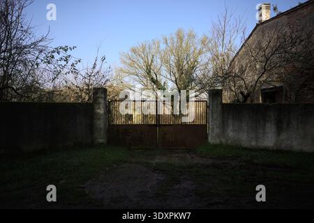 Geschlossenes rostiges Tor in einer Betonmauer, die zu einem Garten führt, auf dem italienischen Land Stockfoto