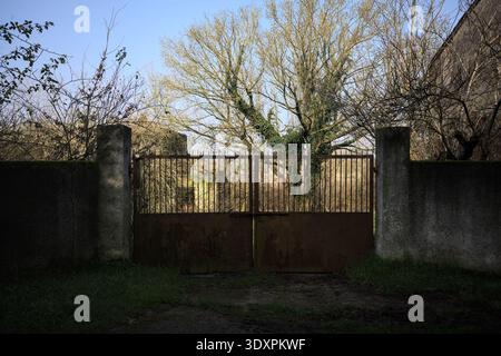 Geschlossenes rostiges Tor in einer Betonmauer, die zu einem Garten führt, auf dem italienischen Land Stockfoto