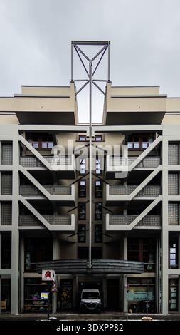 Markantes, symmetrisches, modernistisches Mehrfamilienhaus in Berlin mit zentralem Stahlgitterturm, geometrischen Balkonen und leichten Treppen unter bewölkten s Stockfoto