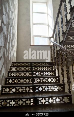 Antike gusseiserne Treppe mit kunstvollen Mustern in einem historischen Gebäude mit einem hellen Fenster. Stockfoto