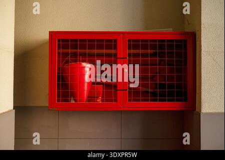 Roter Metallfeuerschutz mit kegelförmigem Eimer und an der Wand montierten Sicherheitswerkzeugen. Stockfoto