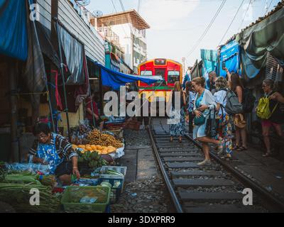 Der Zug fährt durch den Maeklong Railway Market in Samut Songkhram, Thailand, während Händler und Touristen sich von den Bahngleisen entfernen. Stockfoto