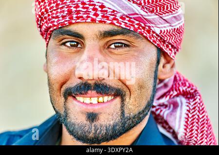 Ein junger Mann lächelt, während er in Syrien ein rot-weißes Kopftuch trägt. Sein Ausdruck zeigt Wärme und Freundlichkeit in einer ungezwungenen Umgebung. Stockfoto