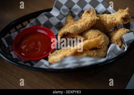 Goldenes frittiertes Essen in schwarzem Korb mit roter Dippsoße auf Papier Stockfoto