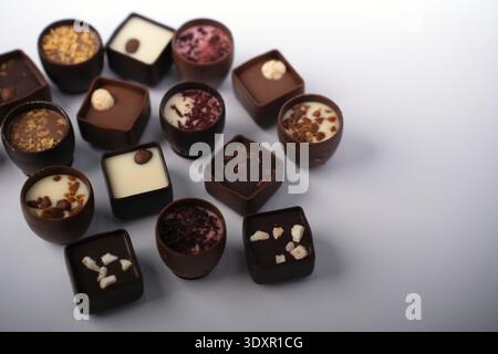 Nahaufnahme mit verschiedenen Gourmet-Schokoladenbonbons und Trüffeln, die auf einem sauberen weißen Tisch im Studio angeordnet sind und glänzendes dunkles und cremiges weiß zeigen Stockfoto