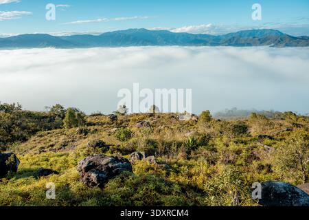 Die Landschaft in großer Höhe zeigt eine atemberaubende Wolkenumkehr über ein riesiges Bergtal. Mit grünen felsigen Hügeln im Vordergrund und weit entfernt Stockfoto
