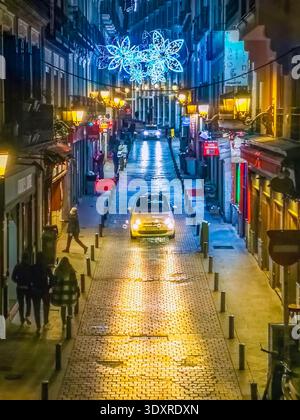Nächtliche Straßenszene in Madrid während der Weihnachtszeit mit festlichen Lichtern, die eine Kopfsteinpflasterstraße beleuchten. Madrid, Spanien - 30. November 2021 Stockfoto