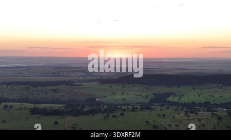 Drohnenlandschaft mit Sonnenaufgang über sanften Weidefeldern und ländlichem Ackerland mit Morgenlicht, das das ländliche Gelände beleuchtet. Stockfoto