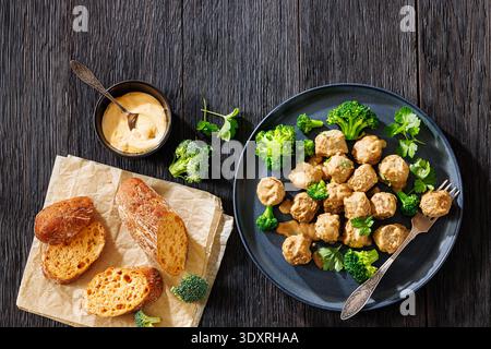 Belgische Gehaktballen, Fleischbällchen in cremebrauner Soße mit gedämpften Brokkoli-Röschen auf Teller mit Gabel, knuspriges Baguette auf dunklem Holztisch, flache Ladefläche, Stockfoto