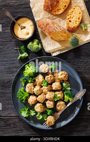 Belgische Gehaktballen, Fleischbällchen in cremebrauner Soße mit gedämpften Brokkoli-Röschen auf Teller mit Gabel, knuspriges glutenfreies Baguette auf dunklem Holztisch Stockfoto