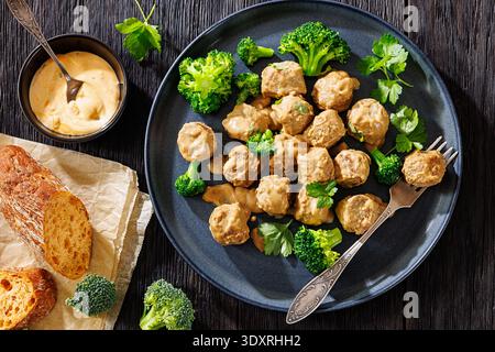 Belgische Gehaktballen, Fleischbällchen in cremebrauner Soße mit gedämpften Brokkoli-Röschen auf Teller mit Gabel, knuspriges glutenfreies Baguette auf dunklem Holztisch Stockfoto