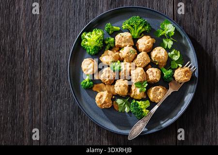 Belgische Gehaktballen, Fleischbällchen in cremebrauner Soße mit gedämpften Brokkoli-Röschen auf Teller mit Gabel auf dunklem Holztisch, flach liegend, freier Platz, kein A Stockfoto