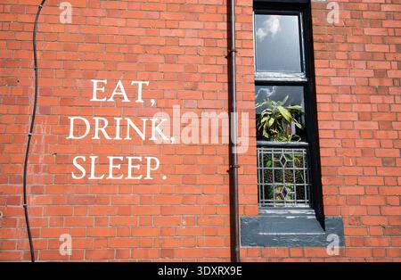 Rote Backsteinaußenwand eines traditionellen Pubs mit den Worten Eat, Drink, Sleep in weiß gemalt. Hospitality Konzept, Essen und Getränke Thema. Stockfoto