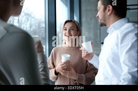 Drei Personen stehen vor einem Fenster, lächeln und halten Tassen Stockfoto