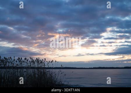 Dramatischer Sonnenaufgangshimmel über dem gefrorenen See mit Schilf Silhouette ruhige Winterlandschaft Stockfoto