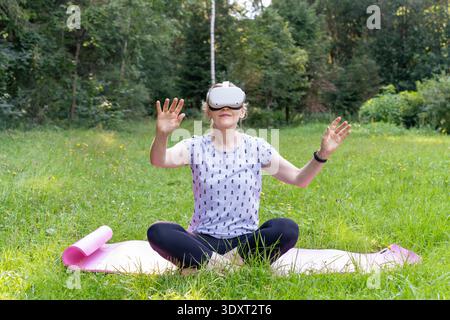 Eine entspannte Frau lächelt, während sie die VR-Technologie nutzt, um praktisch aus einem Waldpark zu reisen. Dieses Konzept hebt den digitalen Eskapismus und den virtuellen Tourismus hervor. Stockfoto