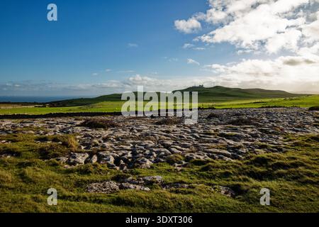 Eine Weite aus freiliegendem Felsen, Kalksteinpflaster; weicht zu sonnendurchfluteten grünen Weiden mit Hügeln im Hintergrund, Llandudno, Nordwales. Stockfoto