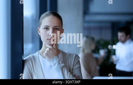 Eine Frau steht vor einem Fenster mit der Hand am Kinn Stockfoto