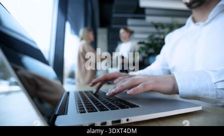 Ein Mann tippt auf einem Laptop vor einem Fenster Stockfoto