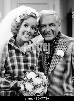 Diese schwarz-weiße Publicity aus den 1970er Jahren zeigt die Schauspieler Georgia Engel und Ted Knight, wahrscheinlich aus ihren Rollen in der Mary Tyler Moore Show um 1975. Engel ist in einem Hochzeitsschleier und kariertem Hemd dargestellt, der einen Blumenstrauß hält, neben einem lächelnden Ritter in einer gemusterten Anzugsjacke mit einer Boutonnière, was auf eine Feier- oder Hochzeitsszene aus der Fernsehserie hindeutet. Stockfoto