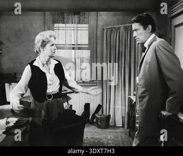 Dieses Vintage-Werbefoto aus dem Jahr 1958 fängt Carroll Baker und Gregory Peck in einer dramatischen Szene aus dem amerikanischen Western-Film „The Big Country“ ein. Baker scheint mit einem besorgten Ausdruck mit Peck zu sprechen, der sich gegen Möbel mit stoischem Aussehen lehnt und die Intensität des Genres betont. Stockfoto