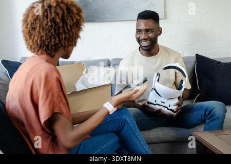 Paarung: Weißes VR-Headset auf dem Sofa, offene Box mit Luftpolsterfolie, Headset halten, Kopierraum Stockfoto
