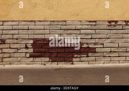 Strukturierter Wandhintergrund mit gelbem Putz und freiliegenden grauen und roten Ziegeln. Stockfoto