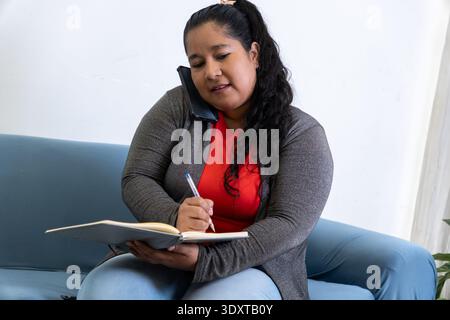 Frau, die telefoniert, während sie in einem Notebook schreibt und von zu Hause aus arbeitet Stockfoto