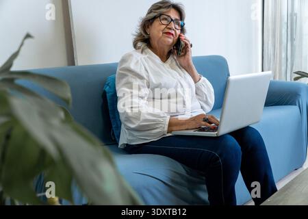 Reife Frau, die von zu Hause aus auf ihrem Sofa kommuniziert und arbeitet Stockfoto