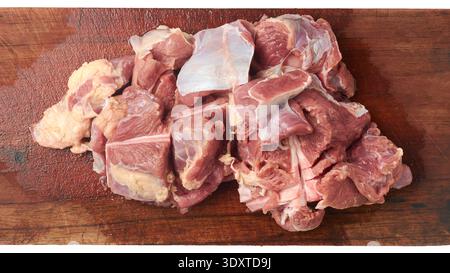 Rohe gehackte Rindfleischstücke auf braunem Holzschneidebrett, feuchte rote Fleischstruktur mit sichtbaren Fett- und Muskelfasern, Blick von oben in der Nähe, kulinarisch Stockfoto