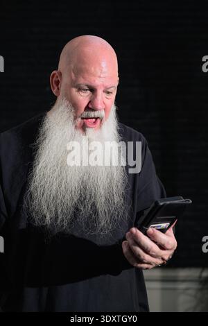 Porträt eines alten Glatzen-Mannes mit langem weißen Bart mit Telefon vor dunklem Hintergrund Stockfoto