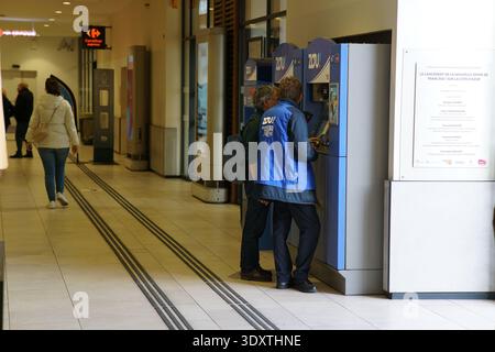 Reisende interagieren mit blauen Gepäckschränken im hellen Korridor des Bahnhofs Nice Ville, und hilfsbereite Mitarbeiter in blauen Westen helfen Ihnen dabei. Nizza Stockfoto