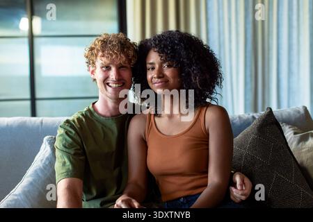 Diverse Paare sitzen auf dem Sofa am Fenster, Mann lächelt in grünem T-Stück, Frau trägt Rosttank Stockfoto
