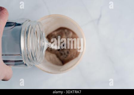 Eine Draufsicht der Hand, die eine Plastikflasche hält und Wasser in einen Shaker mit Proteinpulver gießt Stockfoto