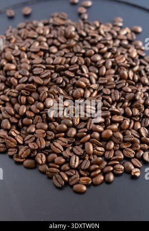 Ein vertikales Hochwinkel-Foto von dunkel gerösteten Kaffeebohnen auf mattschwarzen Hintergrund. Das scharfe Detail im Vordergrund transformiert langsam Stockfoto