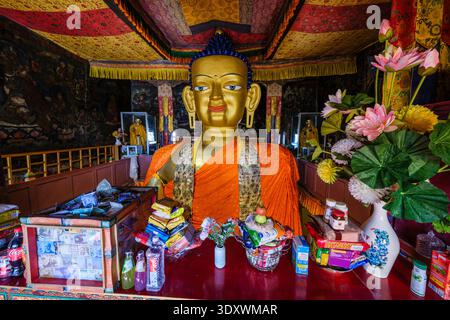 Opfergaben und rituelle Gegenstände werden vor dem monumentalen vergoldeten Shakyamuni Buddha Kopf in der Hauptversammlungshalle in Shey platziert. Stockfoto