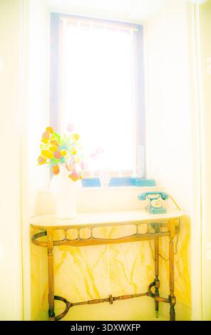 Dekorativer Tisch mit einer Vase aus gelben und rosa Blumen und einem Telefon im Vintage-Stil Stockfoto