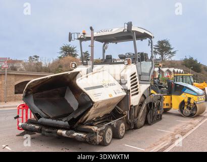 Große Asphaltfertigungsmaschine neben einer gelben Vibrationswalze bei Straßeninstandhaltungsarbeiten in großbritannien, exmouth devon Stockfoto
