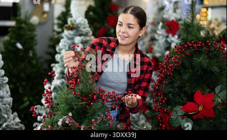 Eine Verkäuferin, die auf dem Weihnachtsmarkt einen künstlichen Weihnachtsbaum mit roten Heidelbeeren dekoriert Stockfoto