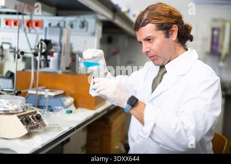 Professioneller lateinischer männlicher Biochemiker zur Untersuchung des Verhaltens blauer flüssiger Reagenzien im modernen Labor Stockfoto