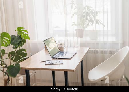 Helles, minimalistisches Home Office mit Laptop auf Holzschreibtisch, bietet komfortable Arbeitsumgebung für ferngesteuerte Arbeit. Home-Office-Arbeitsplatz Stockfoto