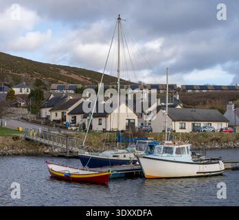 Drei Boote ruhen ruhig im Hafen von Helmsdale. Ein weißes Fischerboot, ein blaues Segelboot und ein kleines rotes Ruderboot sind am Dock gebunden. Stockfoto