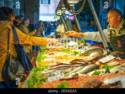 Fischhändler bedient einen Kunden mit frischen Meeresfrüchten auf dem Rialto-Fischmarkt in Venedig, Italien Stockfoto