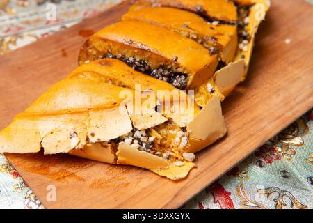 Nahaufnahme der in Scheiben geschnittenen Martabak Manis auf einem Holzteller mit dicker Textur und geschmolzener Schokolade vor einem gemusterten Hintergrund. Stockfoto