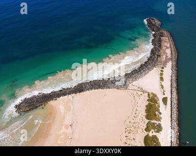 Ein Blick aus der Vogelperspektive zeigt einen Felssteg, wo ruhiges türkisfarbenes Wasser auf das tiefblaue Meer trifft und die Schönheit der Natur unterstreicht. Stockfoto